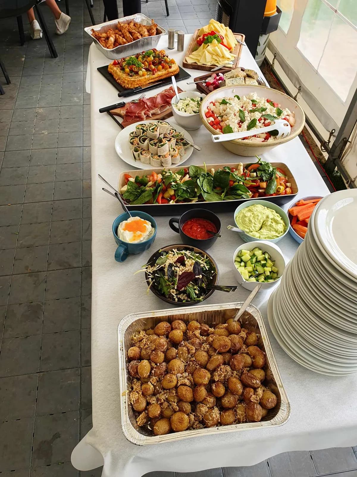 Buffetbord dækket op med salater, tilbehør og stak af tallerkener