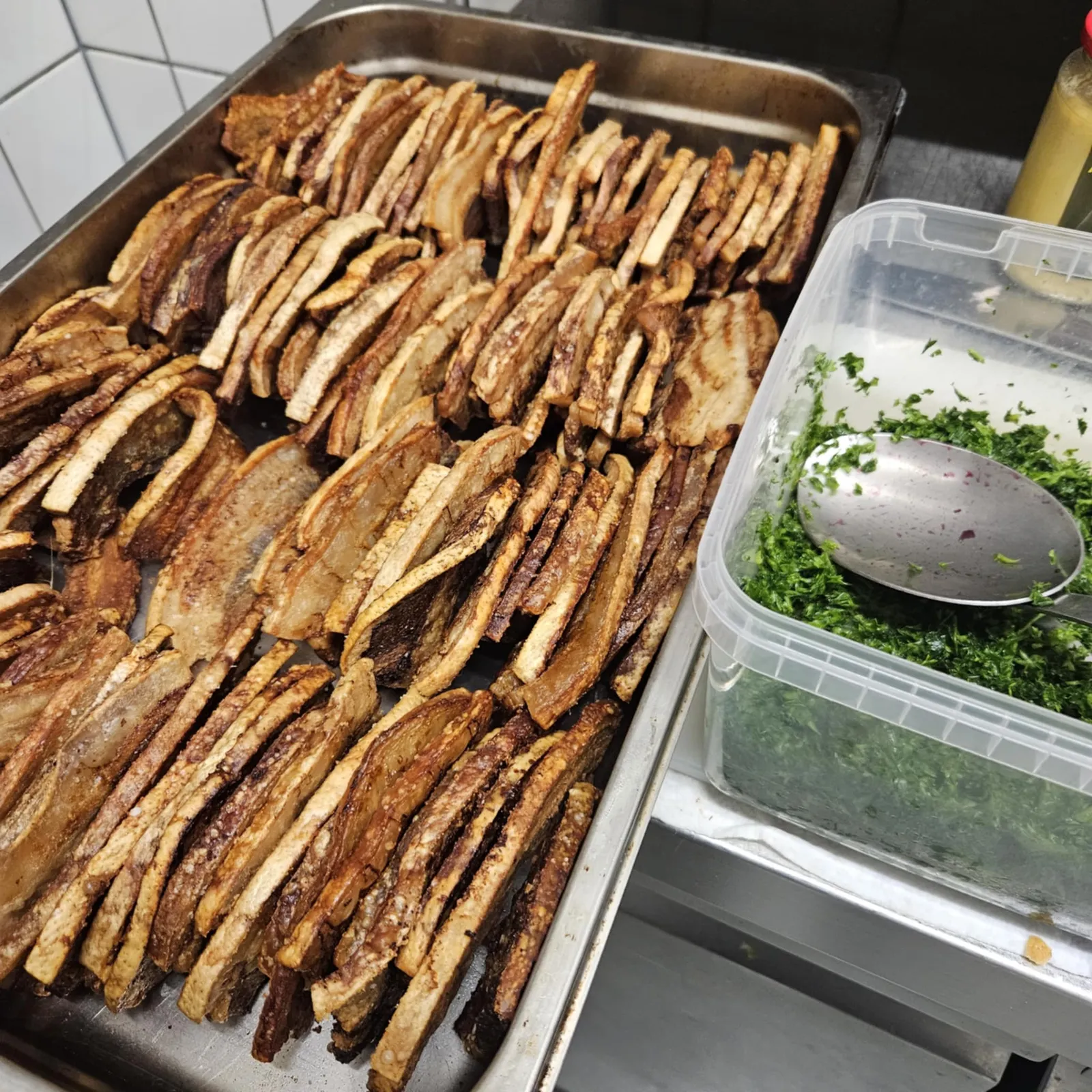 Skiver af grillet kød lagt i buffetbakke med friske krydderurter